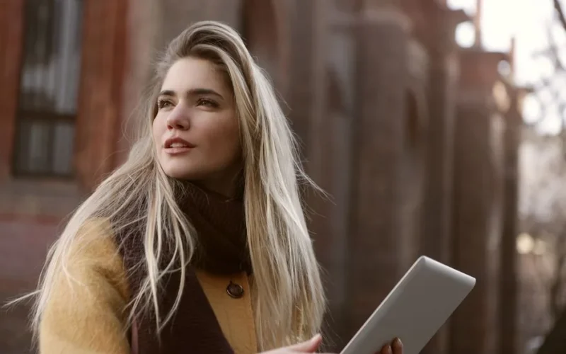 Young woman with long blonde hair holding a tablet outside. Enjoying the view.