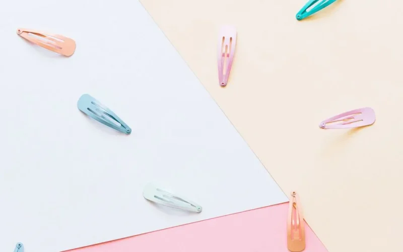 An artistic flat lay featuring colorful hair clips on a pastel geometric background.