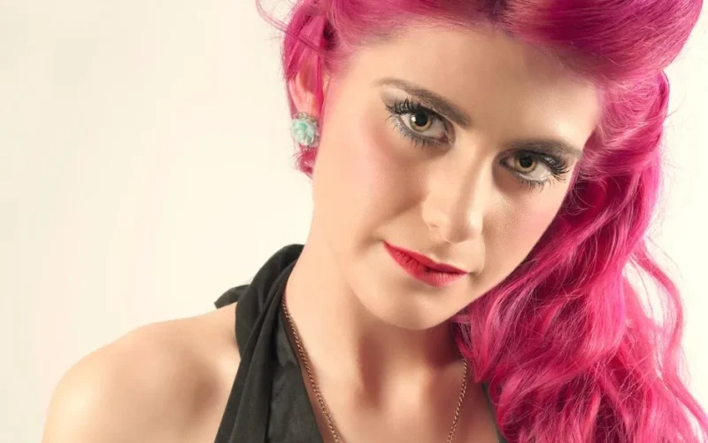 Close-up portrait of a woman with striking pink hair and bold makeup.