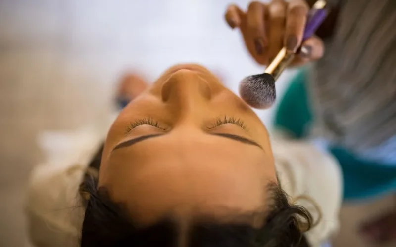 Close-up view of a makeup artist applying blush with a brush to a woman's face.