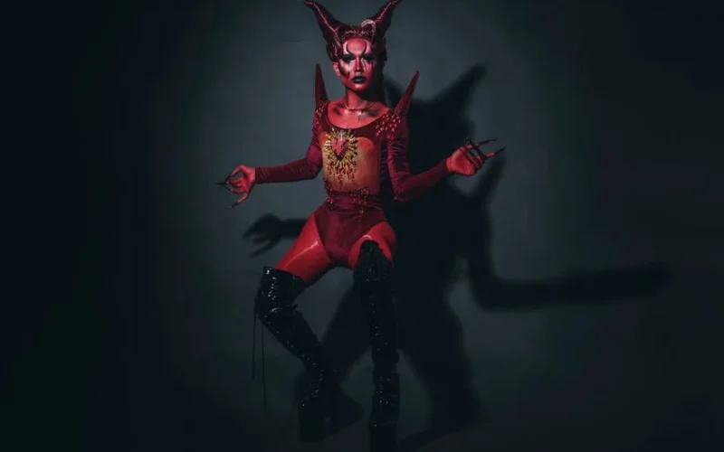 A striking depiction of a woman in a devil costume with body paint and platform boots in a studio setting.