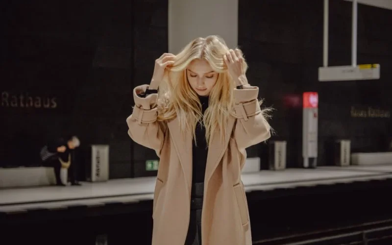 Stylish blonde woman adjusting her hair in an empty urban subway station.