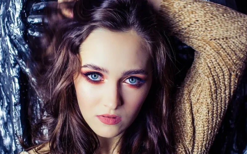 Close-up portrait of a woman with vibrant blue eyes and long hair, posing confidently.