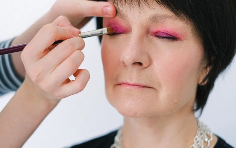 Close-up of a senior woman getting vibrant pink eye makeup applied.