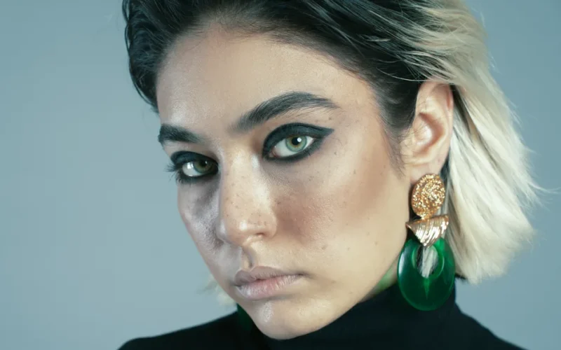 Close-up of an Iranian woman with green eyes, bold makeup, and statement jewelry.
