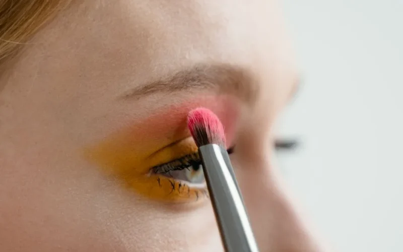 Person applying vibrant eye shadow with a makeup brush for a colorful look.