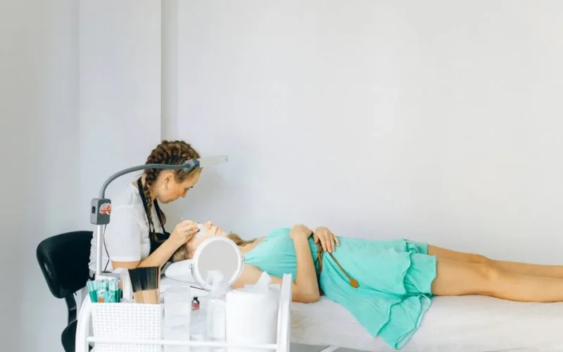 A beautician performing an eyebrow treatment on a client in a modern salon setting.