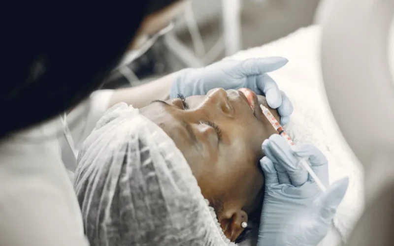 Close-up of a woman receiving a cosmetic lip injection in a clinic setting.