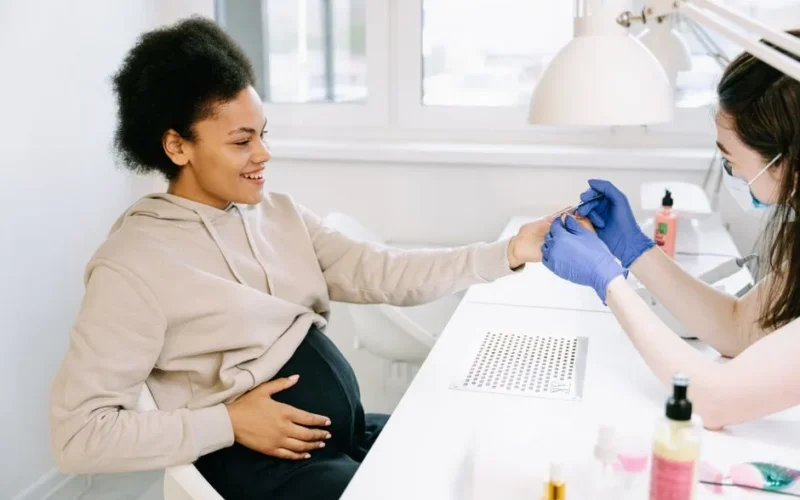 A pregnant woman receives a manicure at a nail salon, highlighting self-care and beauty.