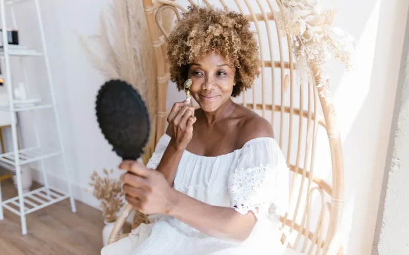 Woman with curly hair applying makeup in a bright indoor setting.