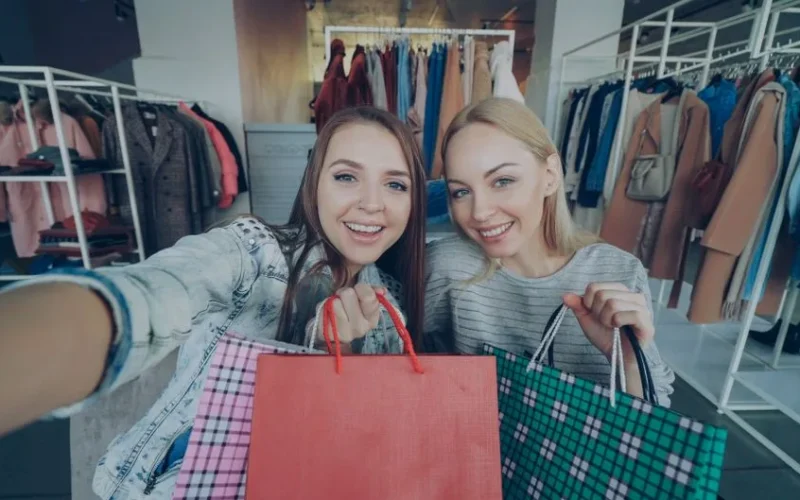 Two smiling women holding shopping bags in a stylish clothing store.