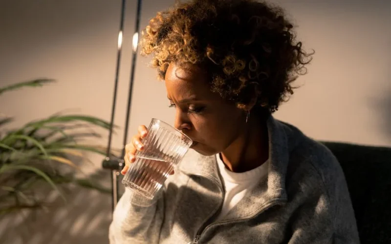 Portrait of an African American woman savoring a refreshing glass of water indoors.