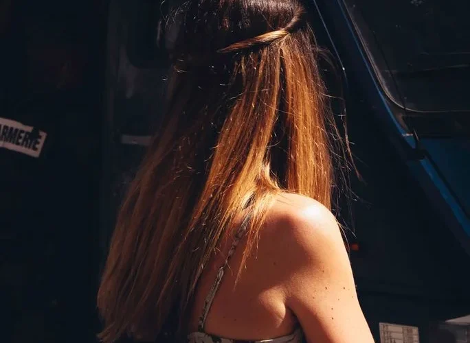A woman with long brown hair stands sunlit in a Paris street, capturing a candid moment.