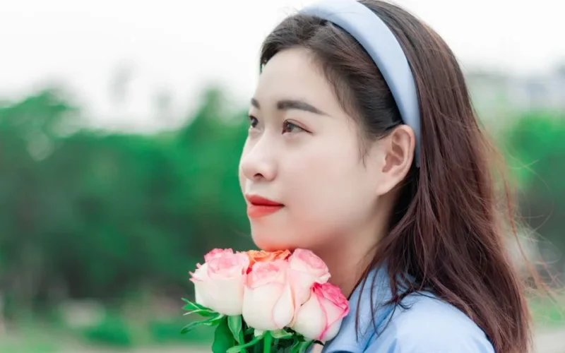 A woman enjoys a serene outdoor moment in spring, holding pink roses and wearing a blue headband.