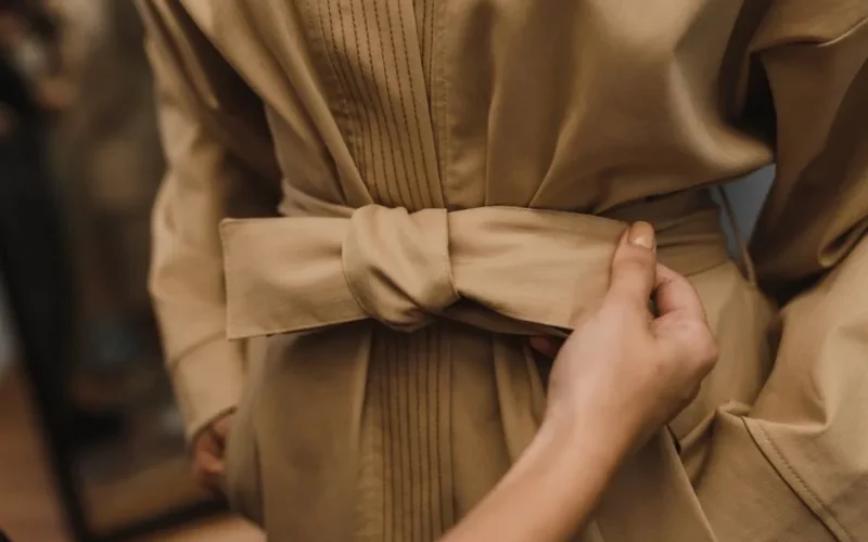 Detail shot of a tan belted coat being tied, highlighting fashion and style.