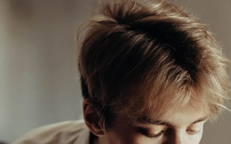 A detailed close-up image showcasing a young man's stylish haircut with tousled, light brown hair.