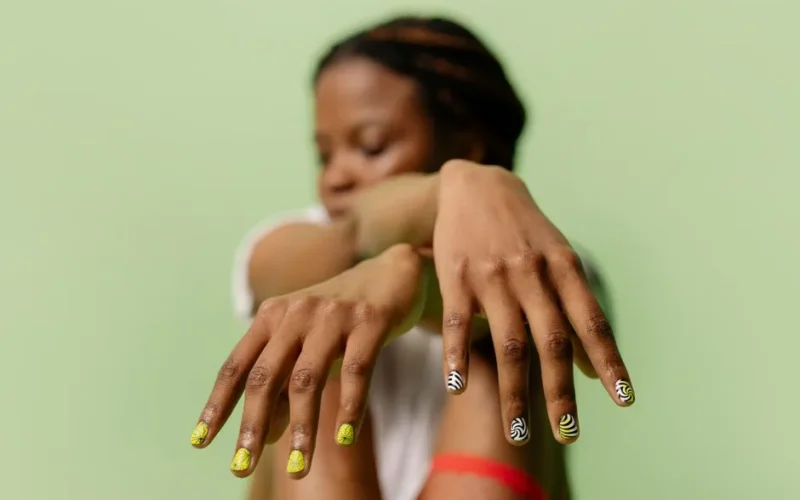 A close-up shot of a woman showcasing intricate nail art designs with a soft green backdrop.