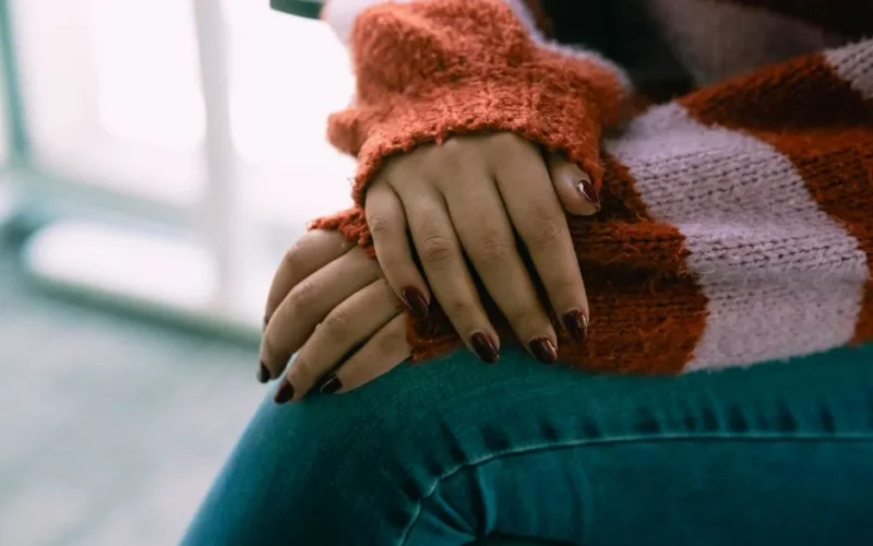Close-up of a woman's hands resting on her lap wearing a warm sweater, conveying comfort and relaxation.