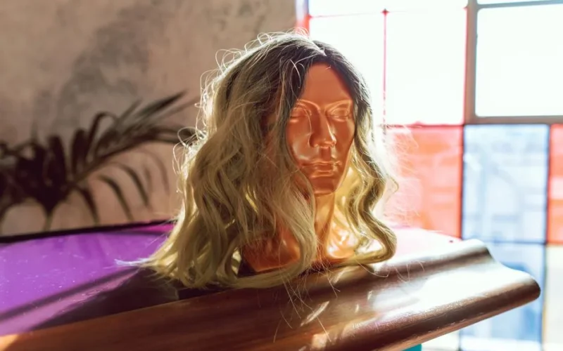 A stylish blonde wig displayed on a mannequin head, illuminated by bright window light.