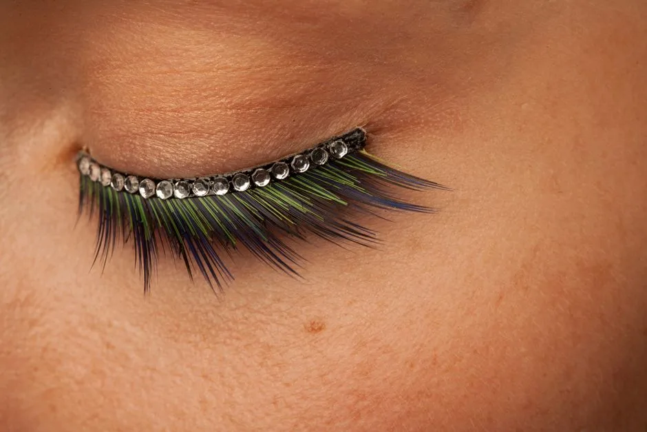 A striking close-up of eyelashes with colorful feathers and rhinestones, showcasing detailed fashion makeup artistry.