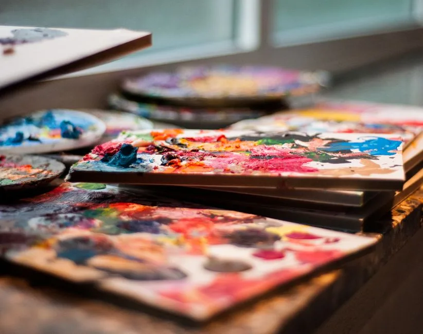 Colorful artist's paint palettes with vibrant hues on a table by the window, creating an inspiring workspace.