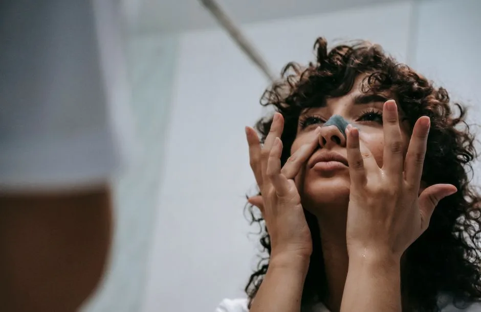 From below of young curly brunette standing in front of mirror and cleansing nose skin with cosmetic strip