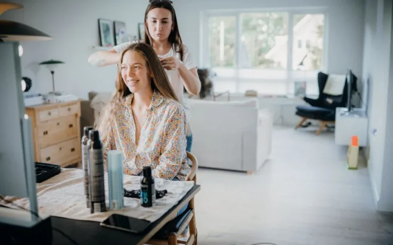 Woman getting her hair styled by a hairdresser in a cozy, sunlit room.