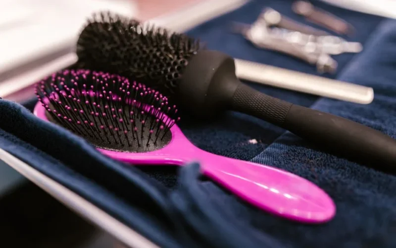Close-up of pink and black hairbrushes on a towel in a salon setting.