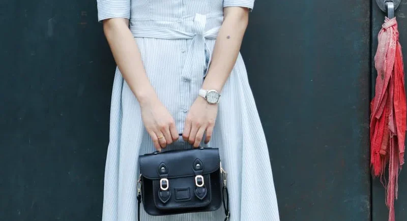 Stylish woman in a striped dress holding a leather handbag against a green door background.