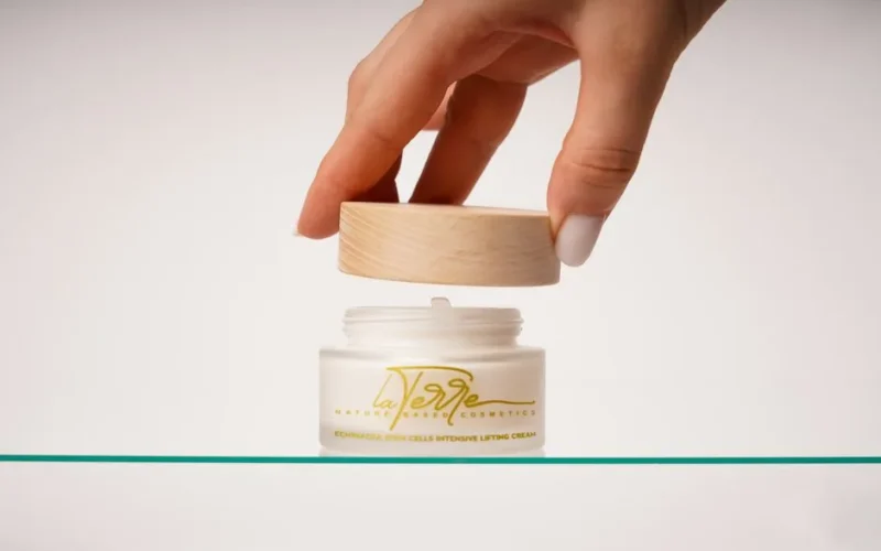 Hand opening Echinacea stem cells lifting cream in minimalist setting.