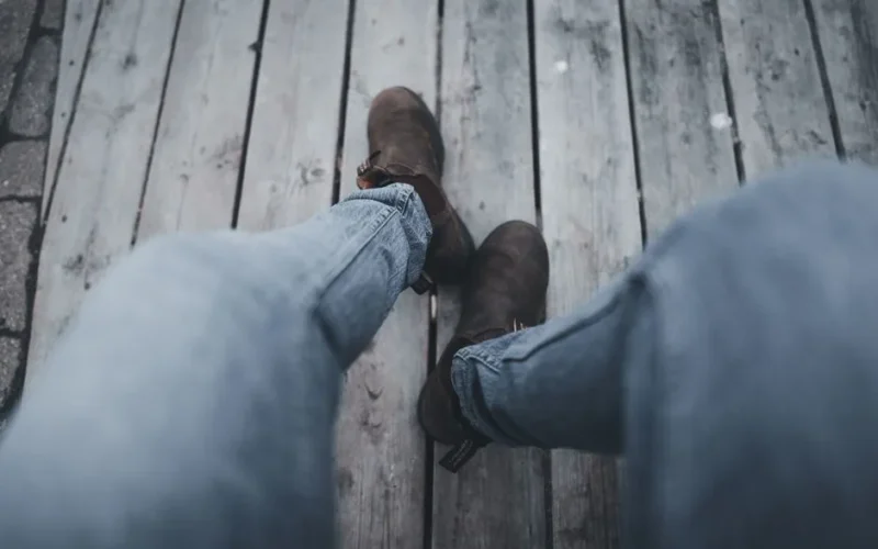 Person sitting outdoors with jeans and brown boots on a wooden floor, casual and relaxed vibe.