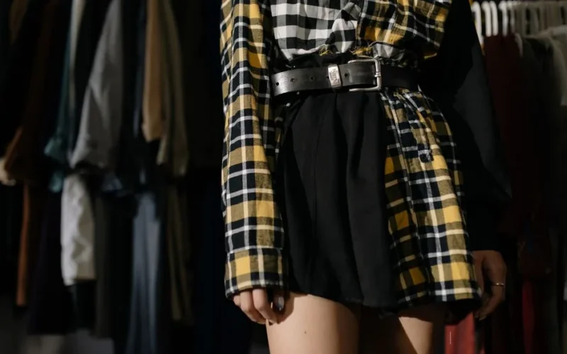 Close-up of a stylish plaid outfit with a belt in a vintage clothing store setting.