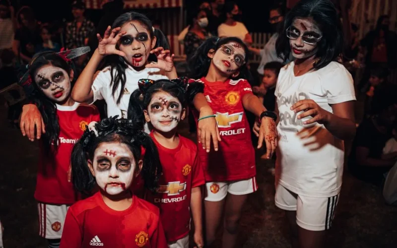 Group of kids in zombie makeup enjoying a Halloween celebration outdoors at night.