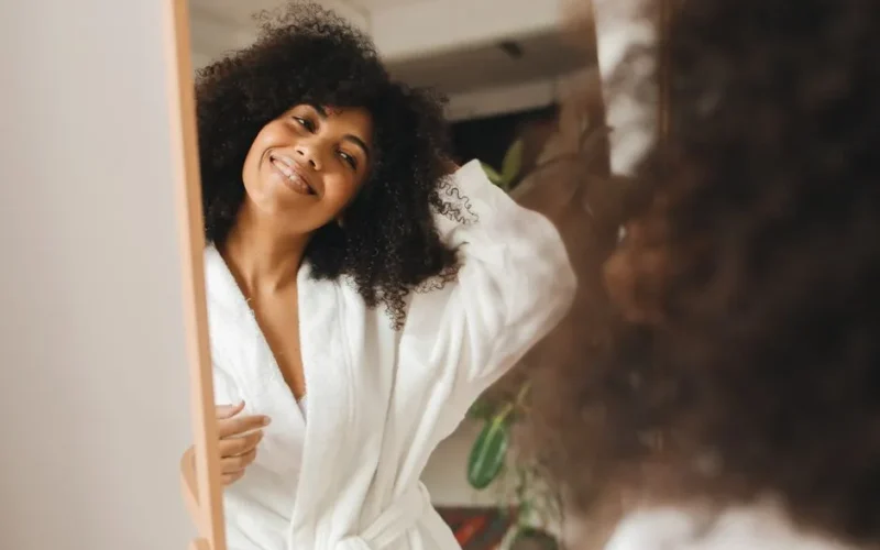 Happy woman with curly hair smiling in a bathrobe at home.