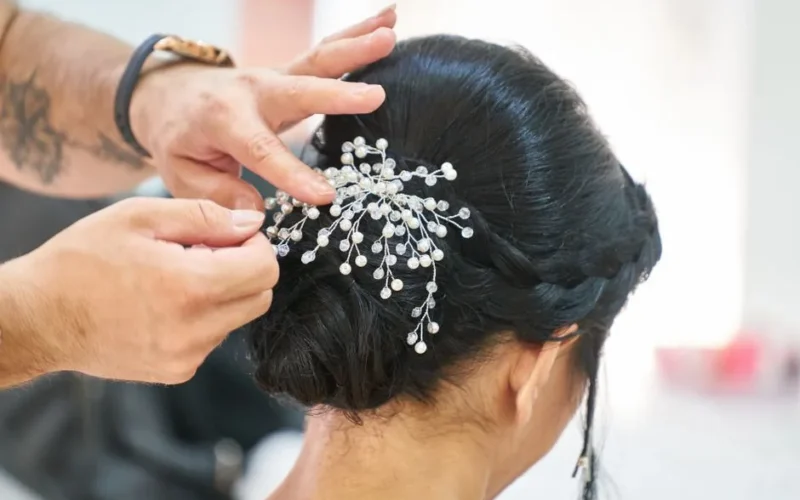 Photograph of a hairstylist arranging an elegant updo embellished with delicate decorative pins in a professional studio.