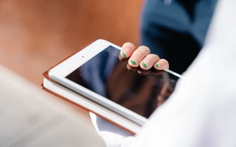 Close-up of a hand with nail polish holding a tablet and notebook. Bright mood.