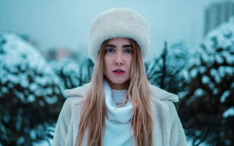 Portrait of a woman in winter attire with a fur hat, white coat, and blonde hair outdoors.