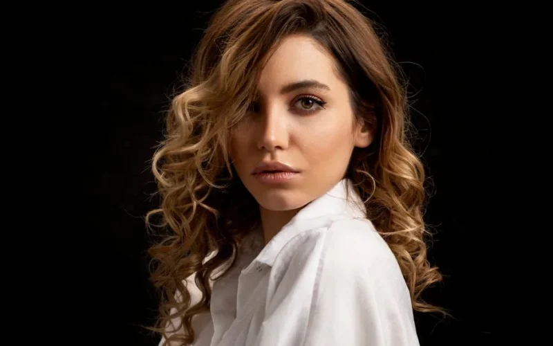 Elegant portrait of a brunette woman with curly hair and a calm expression in a studio setting.