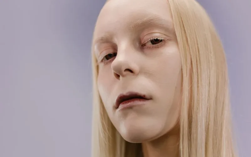 A close-up artistic portrait of a pale young woman with long blonde hair and serene expression.