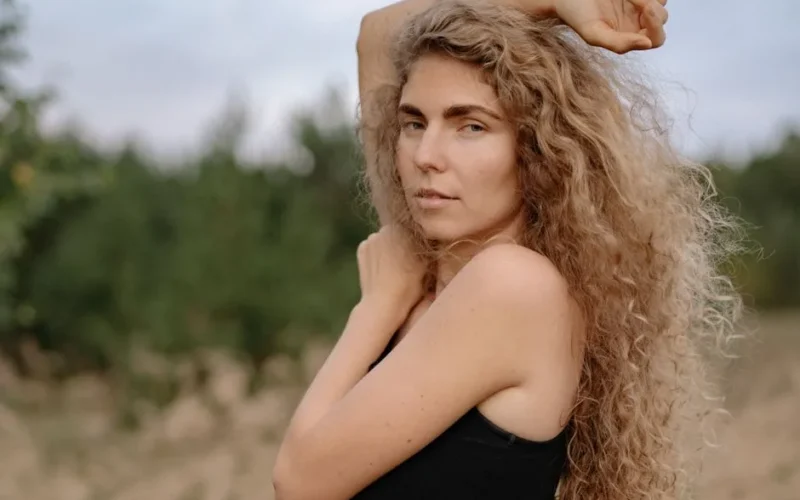 Young woman with long wavy blonde hair posing outdoors in natural light.