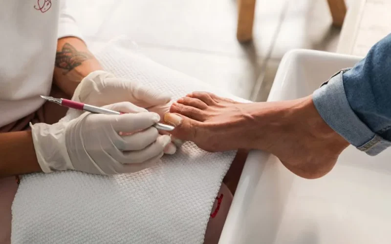 Pedicure session showing gloved hands performing nail care on foot.