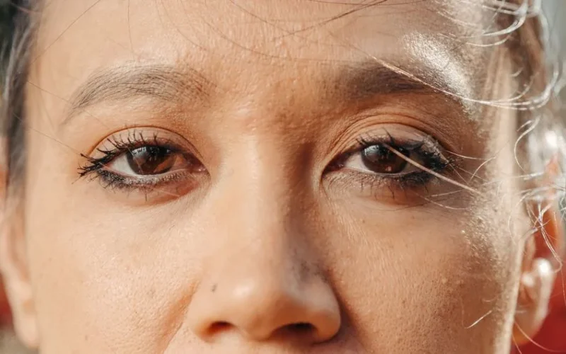 Extreme close-up of a woman's eyes with soft natural lighting, showcasing eye makeup and skin texture.