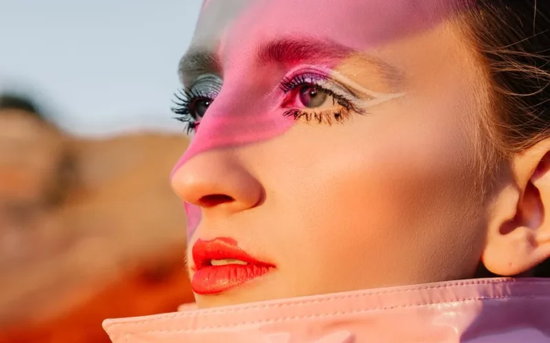 Close-up fashion portrait highlighting vibrant makeup and unique lighting effects.