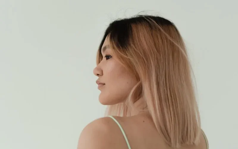 A side view portrait of a woman with light pink balayage hair on a minimalistic background.
