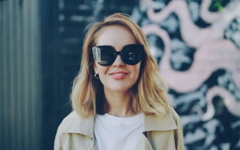 Portrait of a fashionable woman wearing sunglasses, smiling outdoors.