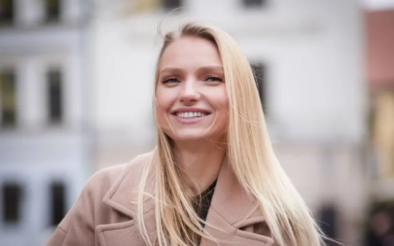 A cheerful adult woman with blonde hair smiling warmly outdoors.