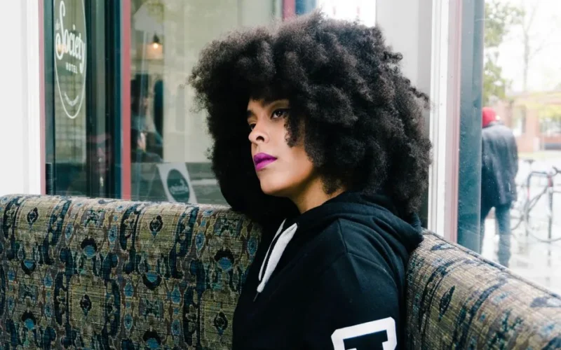 Stylish woman with afro hairstyle sitting in a cafe, exuding beauty and contemplation.