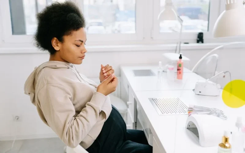 Pregnant woman with afro hair sitting at a nail salon, looking at her manicured nails.