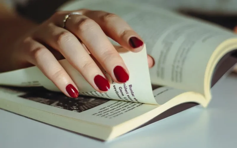 Close-up of a hand with red nails flipping through book pages, showing attention to detail and elegance.