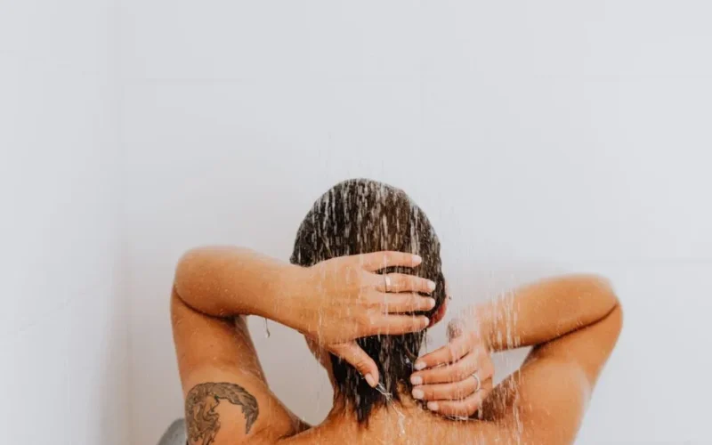 Woman enjoying a soothing shower with water cascading down, emphasizing relaxation and cleanliness.